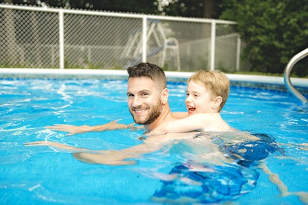 Cute little boy learning to swim with parents in poolの写真素材