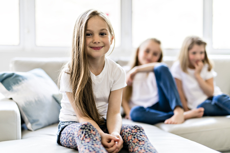 Three attractive child girls in casual clothes watching TV at home