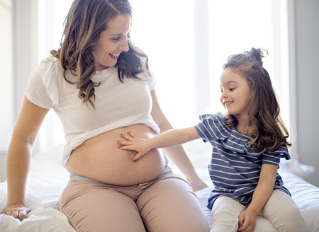pregnant woman with her daughter on bedroom togetherの写真素材