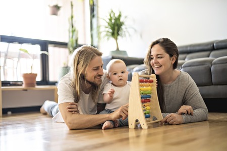 Cheerful parent playing with his baby girl on floor at living roomの写真素材