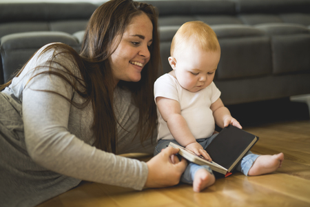 Beautiful woman with her baby and a book in the living roomの写真素材