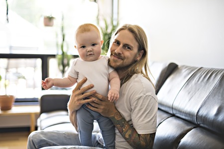 father playing with baby daughter on sofa at home