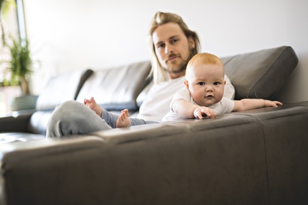 father playing with baby daughter on sofa at homeの写真素材