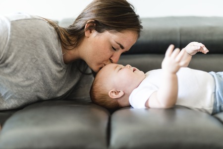 mother with baby daughter on sofa at homeの写真素材