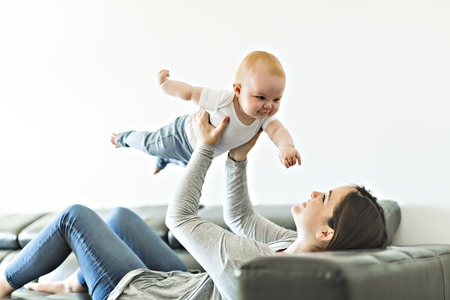 mother with baby daughter on sofa at homeの写真素材