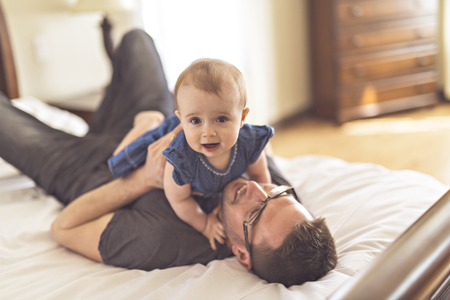 Father playing with her baby in the bedroomの写真素材