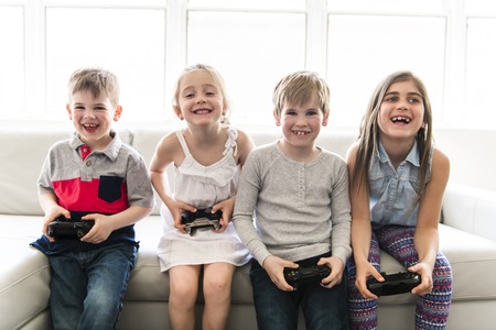 Cheerful kids are sitting together on sofa at home play video gameの写真素材