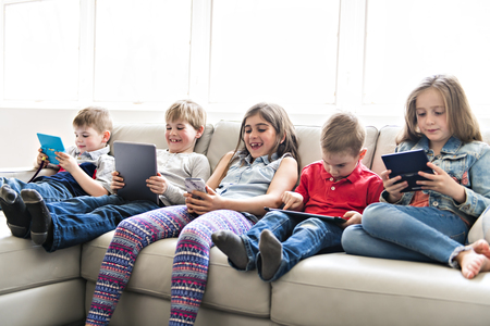 group child Sitting On Sofa At Home With tablet and video gameの写真素材