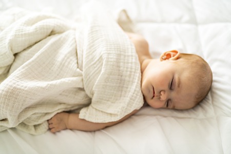 A 4 month baby sleeping on a white bed at homeの写真素材