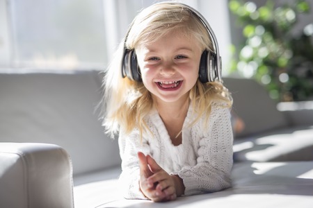 Happy little girl listening music lying on the sofa living-roomの写真素材