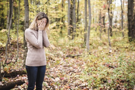 A Sad woman in park during autumn weather hiding face in hand, feeling terrible depressed.の写真素材