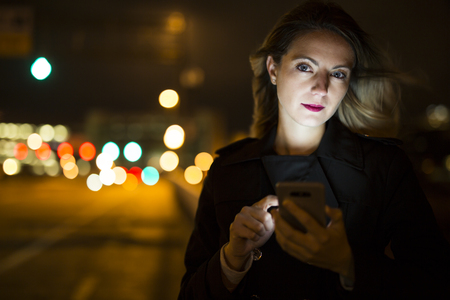 young handsom caucasian woman holding a smartphone on the dark cityの写真素材