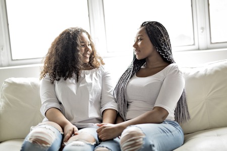 affectionate friends afro american sitting on sofaの写真素材