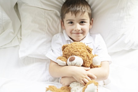 A Child lying in bed with a plush teddy bear