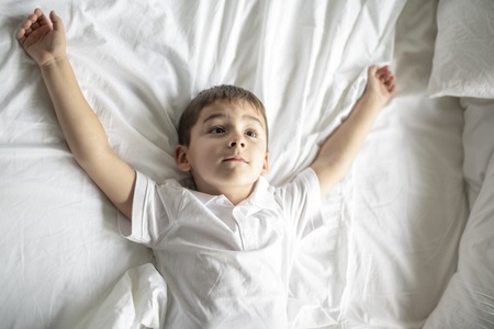 A Little boy lay on the bed with white blanket