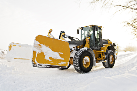 A big yellow snow plow cleaning a road