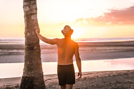 A man with straw hat on the beach at sunset look at the sunsetの写真素材