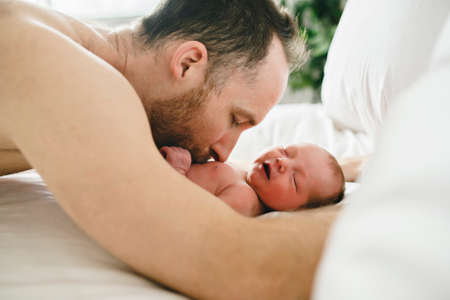 A father with a newborn baby in bed
