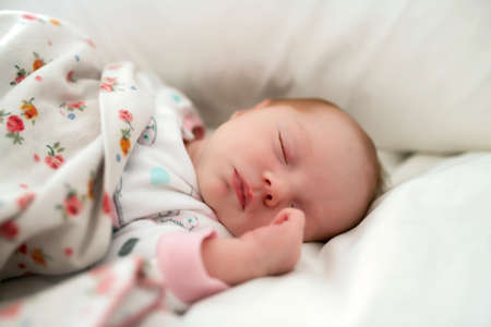 A Sweet newborn baby girl sleeping in white bedの写真素材