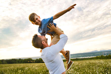 happy family of father and child on field at the sunset having fun flying in the airの写真素材