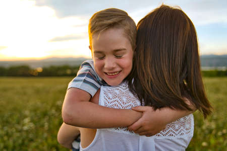 happy family of mother and child on field at the sunset having fun giving hugの写真素材