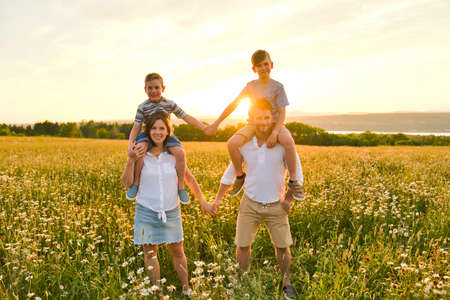 Happy family on daisy field at the sunset having great time togetherの写真素材