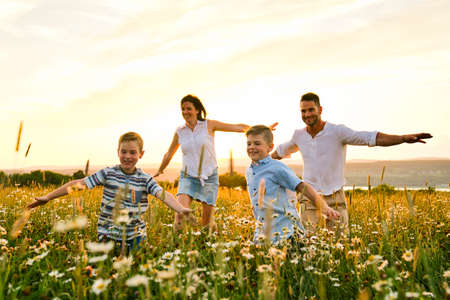 Happy family on daisy field at the sunset having great time together running and flyの写真素材