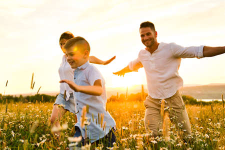 Happy family on daisy field at the sunset having great time together running and flyの写真素材