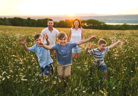 Happy family on daisy field at the sunset having great time together running togetherの写真素材