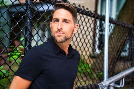 Portrait of a trendy young man close to a fence in the city