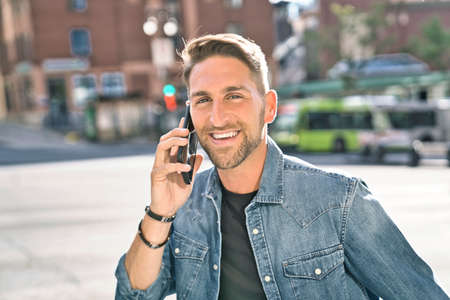 portrait of a trendy young man in the city walking with his phone