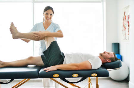 physiotherapist doing treatment with patient in bright office with leg training