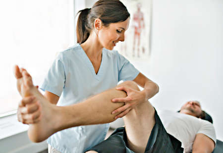 physiotherapist doing treatment with patient in bright office with leg trainingの写真素材