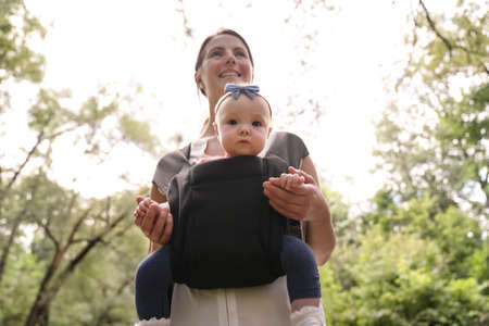 Young beautiful caring mother holding her baby child in a sling walking on natureの写真素材