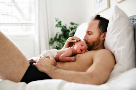 A father with a newborn baby in bed