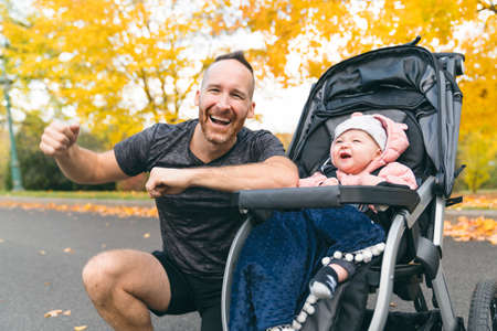 man with her daughter standing in jogging stroller outside in autumn natureの写真素材