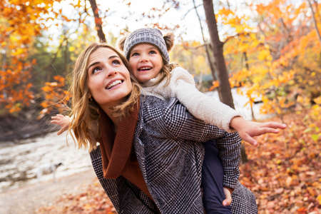 Little girl and her mother playing in the autumn park with child on back