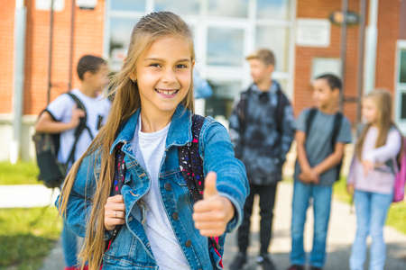 A cute child girl on the first day of school class with a thumb up positive.