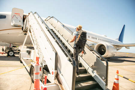 A Young traveling man get in the plane with passport on the landing stripの写真素材