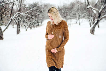 Young happy pregnant woman in snowy forest