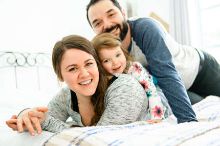 A Happy family, mother, father and daughter on the white bedの写真素材