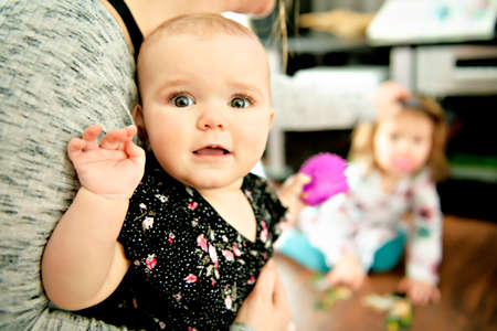 portrait of a happy mother with cute baby at home with sister on the backの写真素材