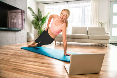Portrait of fit woman training in her living room with laptop