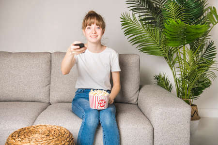 One happy teen watching tv and eating popcorn at homeの写真素材