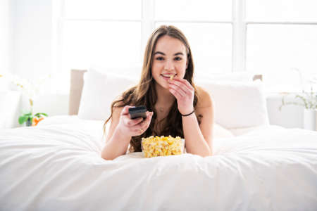 A young teenager watching movies in bed with popcornの写真素材