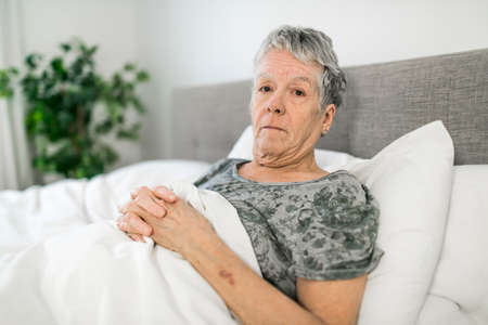 Senior aged woman on bed at home feeling sadの写真素材