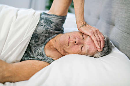 Senior aged woman on bed at home feeling sadの写真素材
