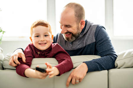 Father with redhead child sit on the sofa at home listening tv