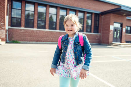 A portrait of trisomie 21 child girl outside on a school playground