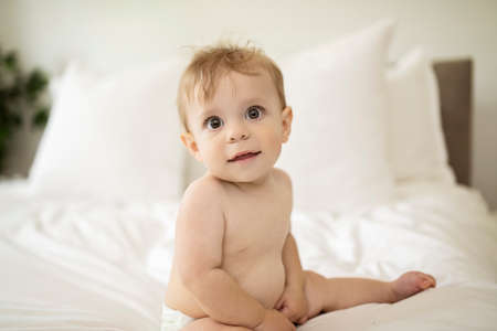 Cute happy baby boy in diaper on bed